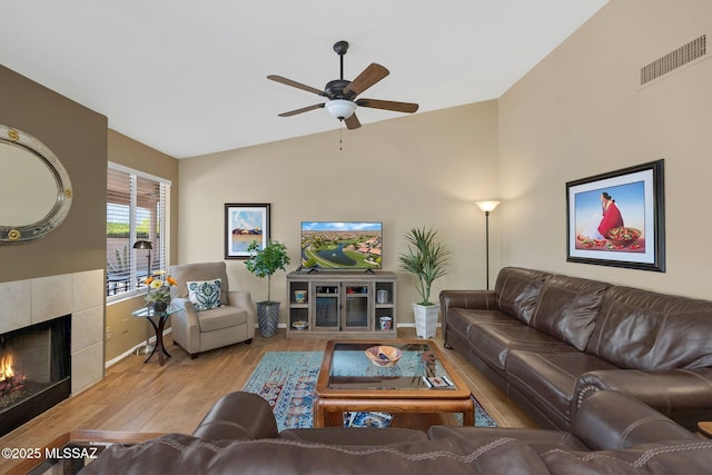 living area with lofted ceiling, ceiling fan, visible vents, wood finished floors, and a tile fireplace