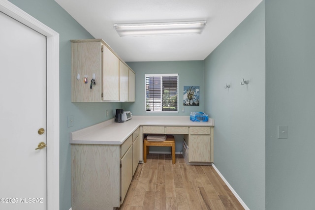 office area featuring light wood finished floors, built in desk, and baseboards