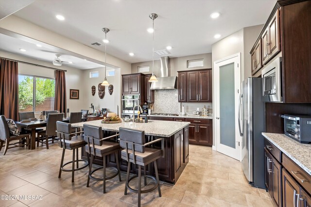660 W Aviator Crossing Dr, Oro Valley, AZ 85755 - kitchen featuring wall chimney range hood, dark brown cabinets, appliances with stainless steel finishes, a kitchen breakfast bar, and an island with sink