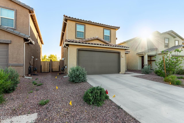 mediterranean / spanish-style home featuring stucco siding, a gate, a tile roof, concrete driveway, and an attached garage