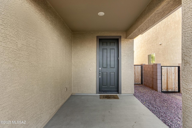 doorway to property featuring fence, stucco siding, and a gate