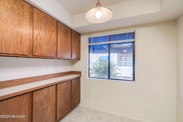 kitchen with baseboards, light tile patterned floors, light countertops, and brown cabinets