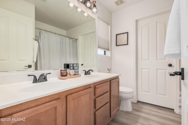bathroom featuring toilet, visible vents, a sink, and wood finished floors