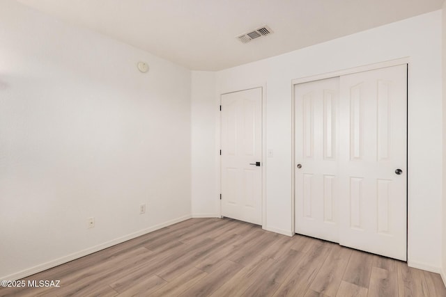 unfurnished bedroom with a closet, light wood-style floors, visible vents, and baseboards