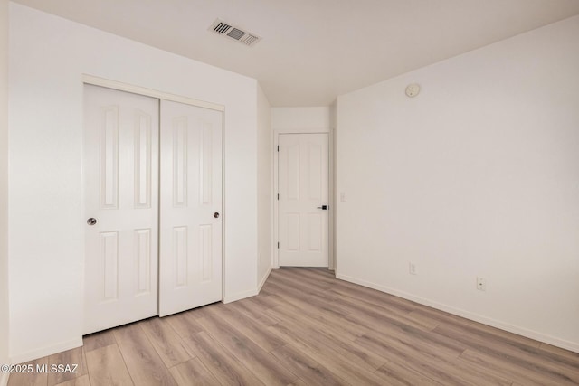 unfurnished bedroom with baseboards, a closet, light wood-style flooring, and visible vents