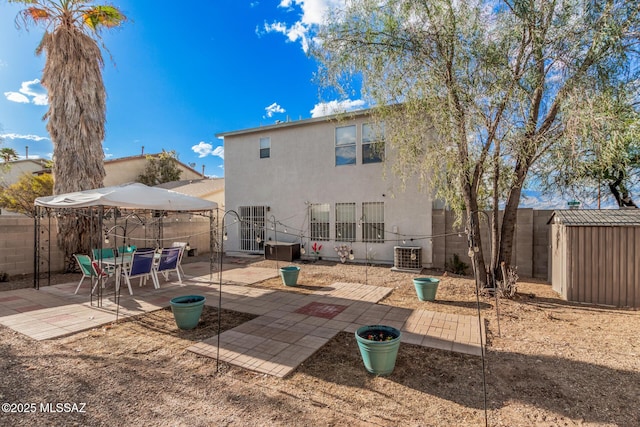 back of property featuring a storage unit, a patio, stucco siding, a fenced backyard, and central AC unit