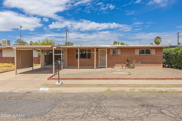 ranch-style home with brick siding, driveway, central AC unit, and an attached carport