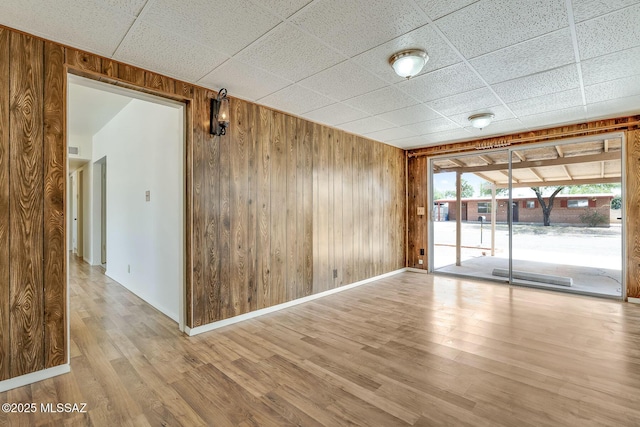 empty room with baseboards, a drop ceiling, wood finished floors, and wooden walls