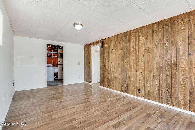 unfurnished room featuring a paneled ceiling, wooden walls, wood finished floors, and washer / clothes dryer