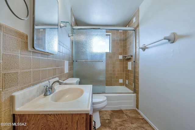 full bath with toilet, vanity, bath / shower combo with glass door, and tile walls