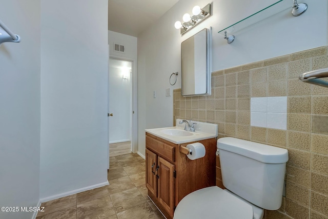 half bath with tile walls, visible vents, vanity, and toilet