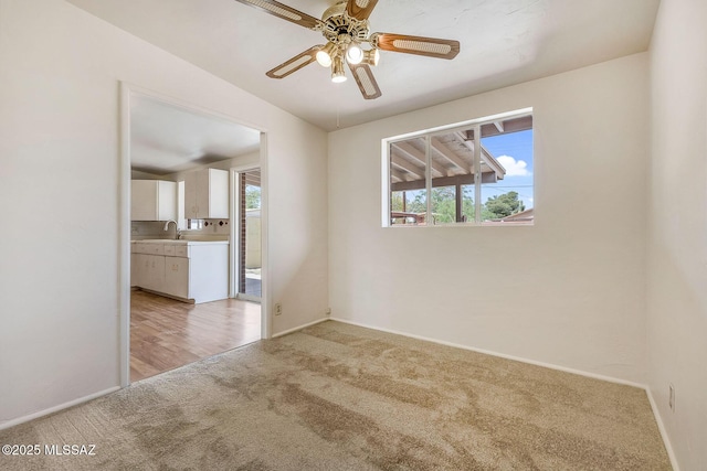 spare room with light carpet, a ceiling fan, baseboards, and a sink