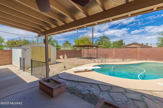 view of swimming pool featuring a storage shed, an outbuilding, a fenced backyard, a diving board, and a patio