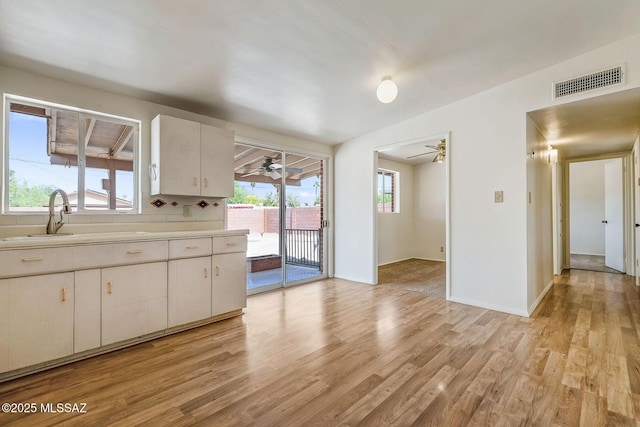 kitchen featuring a ceiling fan, a sink, light wood finished floors, light countertops, and visible vents