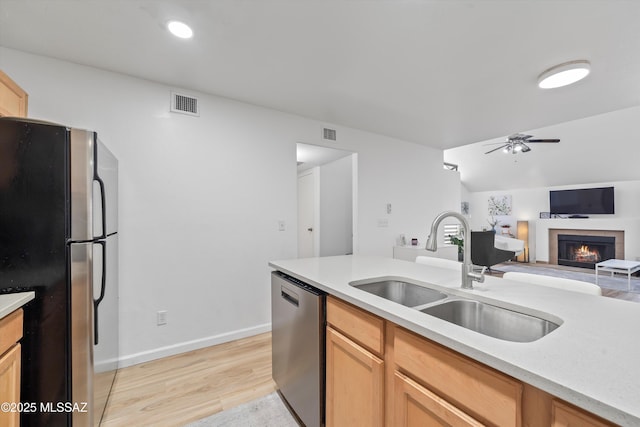 5675 N Camino Esplendora Unit 7-141, Tucson, AZ 85718 - kitchen featuring a sink, stainless steel appliances, a fireplace, ceiling fan, and light wood-style flooring