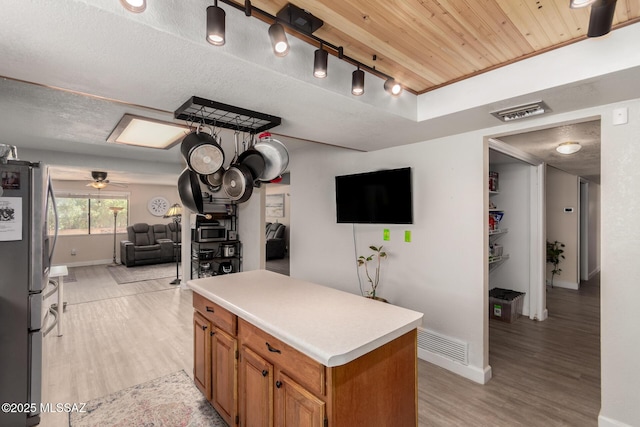 kitchen with brown cabinetry, a kitchen island, baseboards, freestanding refrigerator, and light wood-style flooring