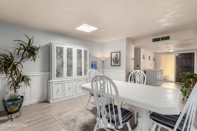 dining room featuring a skylight, wainscoting, light wood finished floors, and visible vents