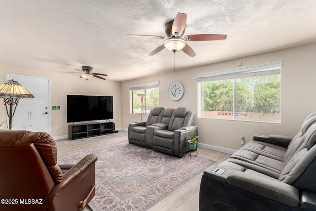 living room with baseboards, ceiling fan, light wood-style flooring, and a textured ceiling