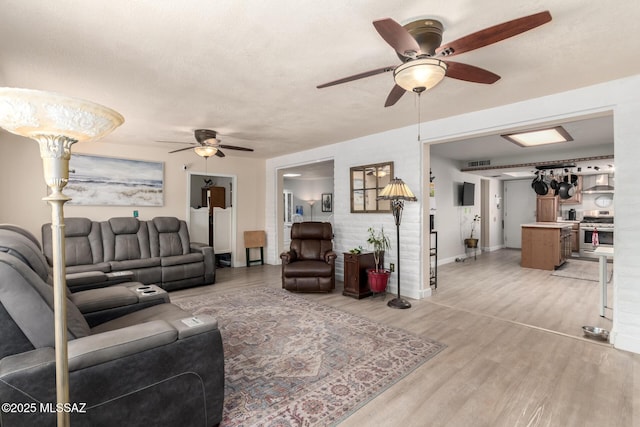 living area with visible vents, a ceiling fan, light wood finished floors, and baseboards