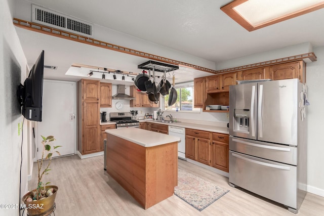 kitchen featuring appliances with stainless steel finishes, a sink, light wood-style floors, wall chimney exhaust hood, and visible vents