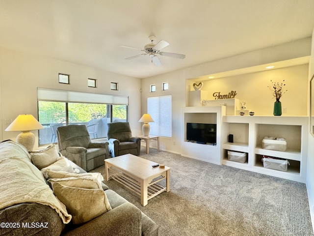 living area featuring baseboards, carpet flooring, built in shelves, and ceiling fan