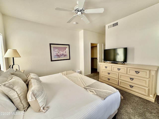 bedroom featuring dark carpet, visible vents, a ceiling fan, a walk in closet, and baseboards