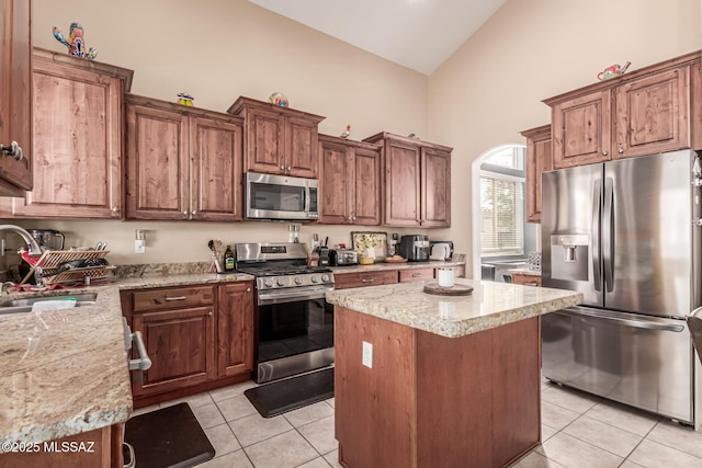 kitchen with a sink, light tile patterned floors, high vaulted ceiling, a center island, and appliances with stainless steel finishes