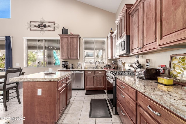 kitchen featuring stainless steel appliances, light tile patterned floors, high vaulted ceiling, a center island, and light stone counters