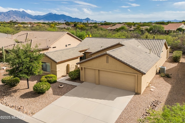 view of front of home featuring concrete driveway, a mountain view, cooling unit, a garage, and stucco siding