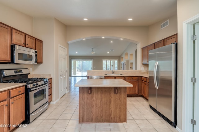 kitchen with stainless steel appliances, arched walkways, a sink, visible vents, and brown cabinetry