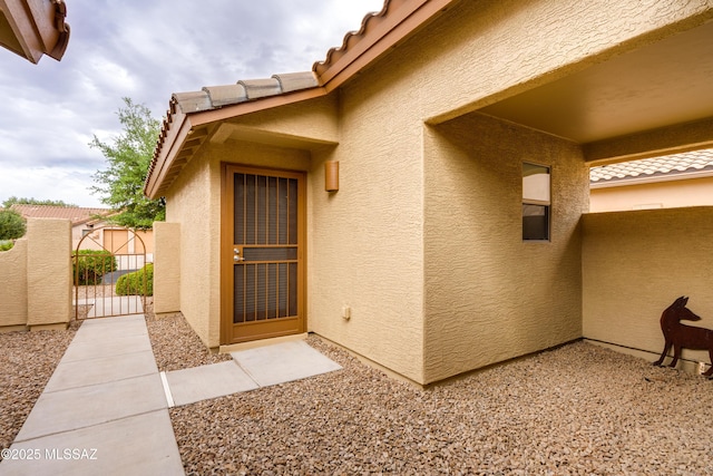 property entrance with a gate, a tiled roof, stucco siding, and fence