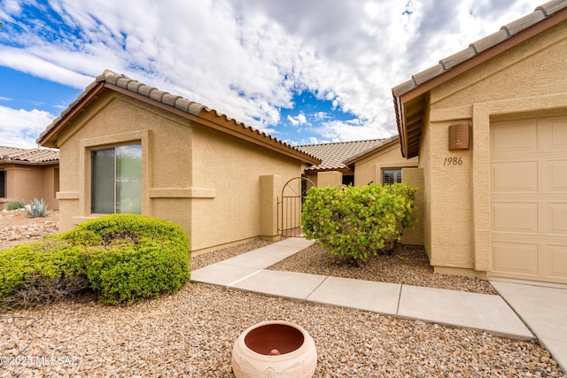 view of side of property featuring a gate, an attached garage, a tiled roof, and stucco siding