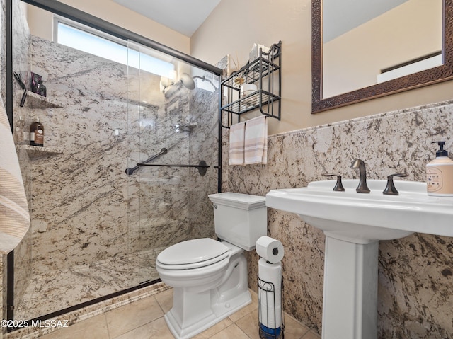 full bath featuring a shower stall, toilet, tile walls, tile patterned flooring, and wainscoting