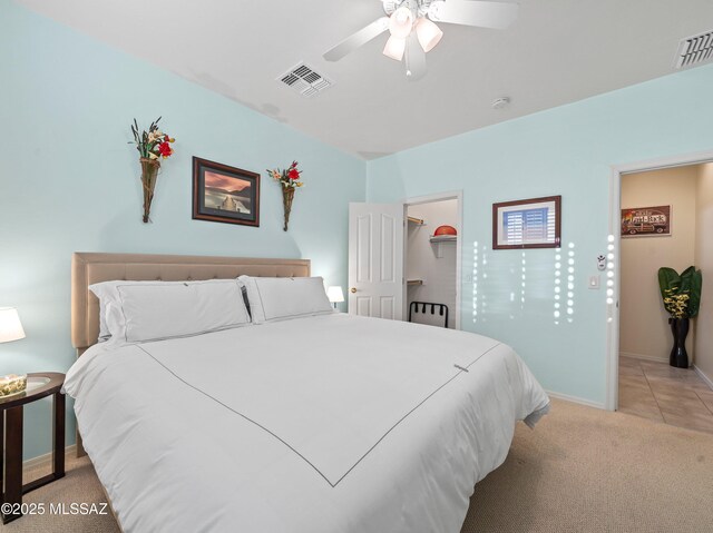 bedroom with visible vents, baseboards, a walk in closet, and light carpet