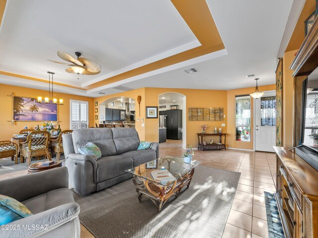 living room featuring arched walkways, plenty of natural light, ceiling fan with notable chandelier, visible vents, and a raised ceiling
