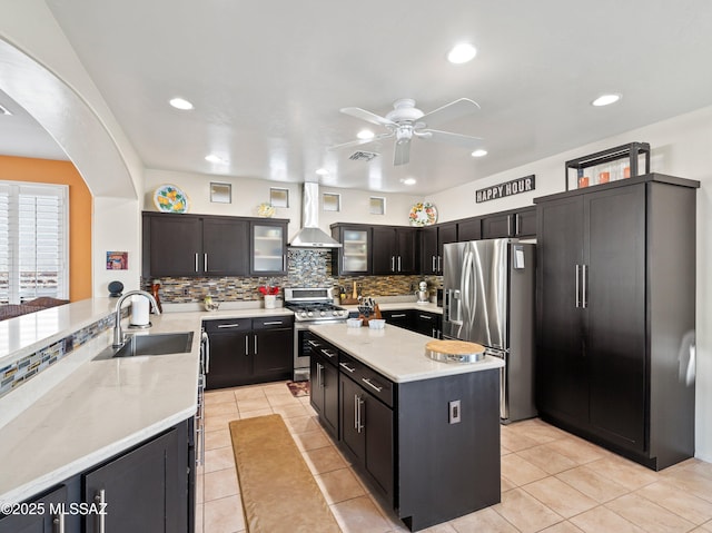 kitchen featuring a sink, tasteful backsplash, a ceiling fan, wall chimney range hood, and appliances with stainless steel finishes