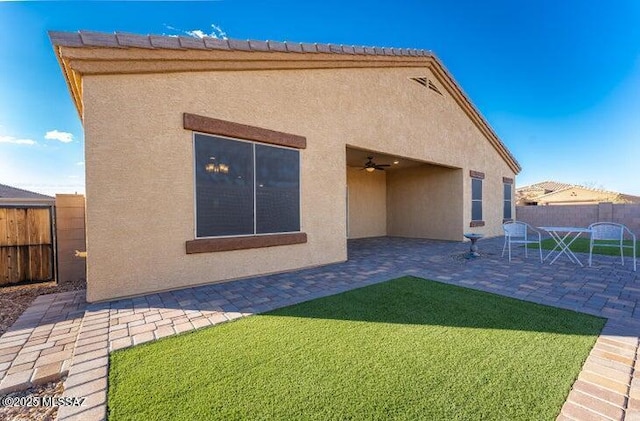 rear view of house featuring a ceiling fan, a fenced backyard, a yard, stucco siding, and a patio