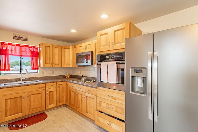 kitchen with recessed lighting, dark countertops, a sink, light wood-style floors, and appliances with stainless steel finishes