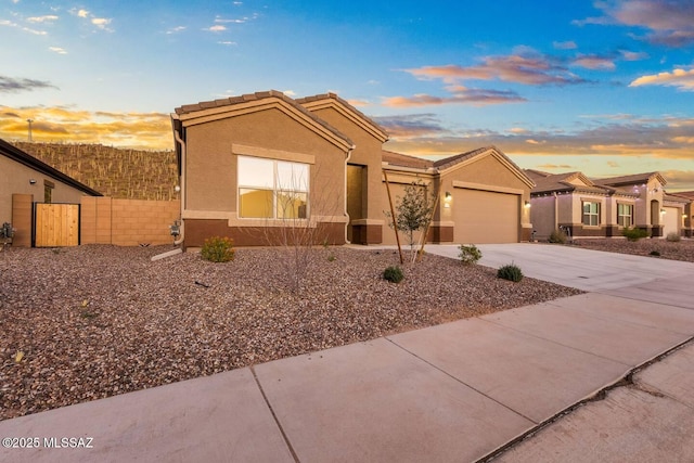 view of front facade featuring a tiled roof, concrete driveway, fence, a garage, and stucco siding