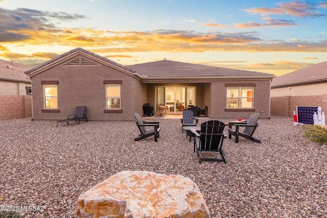 rear view of property featuring a patio area, a tiled roof, an outdoor fire pit, a fenced backyard, and stucco siding
