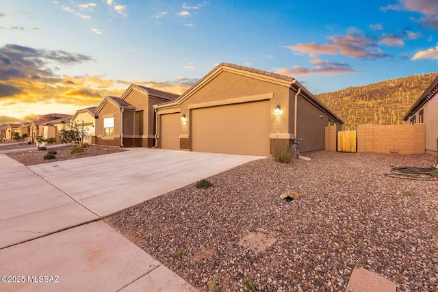ranch-style home featuring fence, a tiled roof, concrete driveway, stucco siding, and a garage