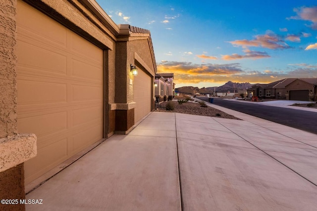 property exterior at dusk with a tiled roof, driveway, a residential view, and stucco siding