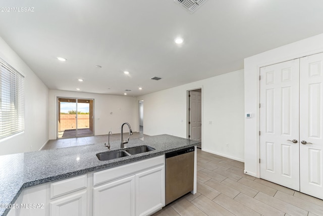 kitchen with dark stone countertops, dishwasher, visible vents, a sink, and white cabinetry