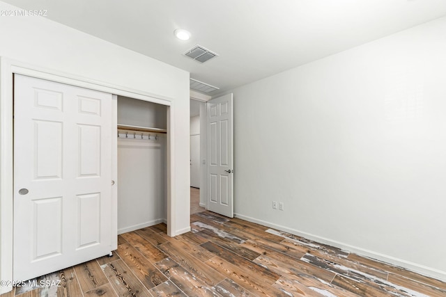 unfurnished bedroom featuring a closet, wood finished floors, visible vents, and baseboards