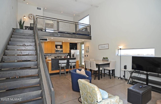 living area with a towering ceiling, stairs, finished concrete floors, and visible vents