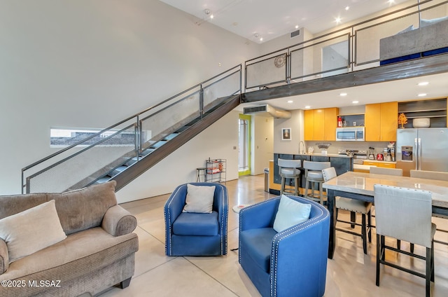 living area with visible vents, concrete flooring, stairs, and a towering ceiling