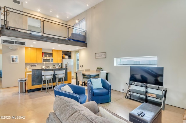 living room featuring concrete flooring, a high ceiling, visible vents, and bar