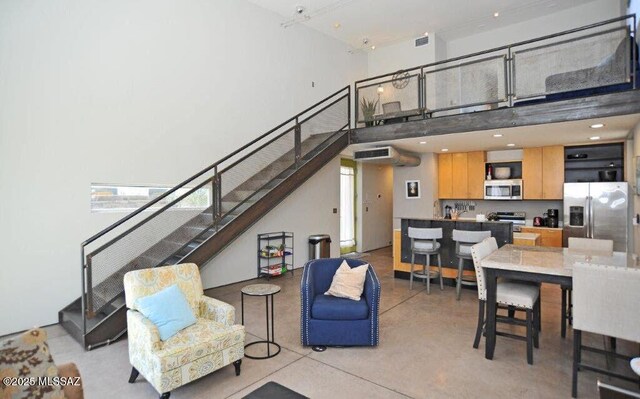 living area featuring concrete floors, stairs, visible vents, and a towering ceiling