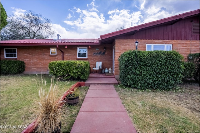 view of front of property featuring brick siding, metal roof, and a front yard