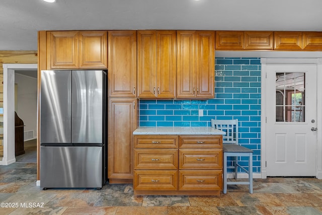 kitchen featuring visible vents, freestanding refrigerator, stone finish flooring, brown cabinetry, and light countertops